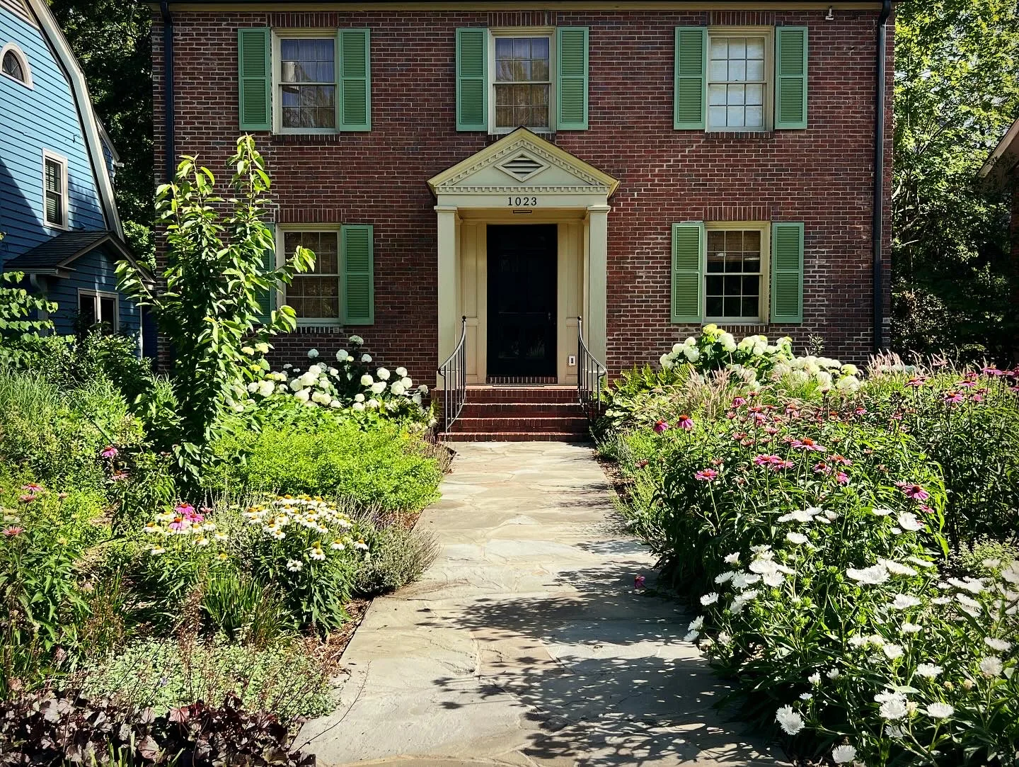 A brick home with a stone walk framed by deep perennial borders