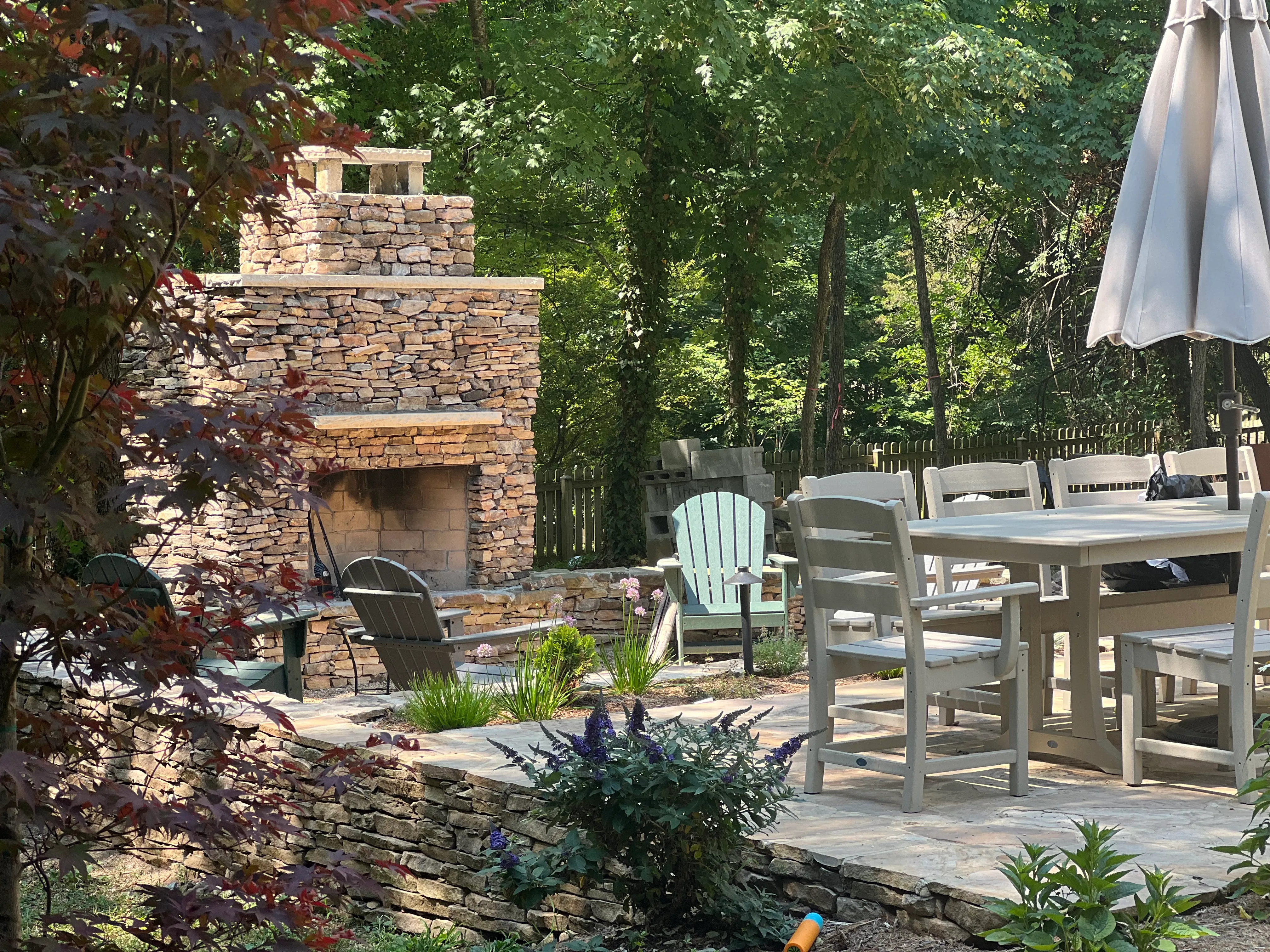 A stone patio with an outdoor fireplace and dry-stack retaining wall